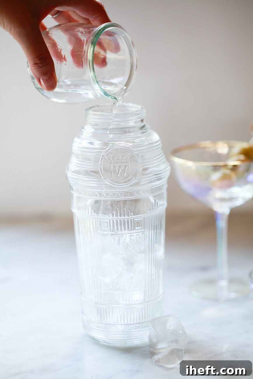 A small glass filled with 2.5 ounces of gin or vodka is poured into a vintage crystal cocktail shaker filled with ice.