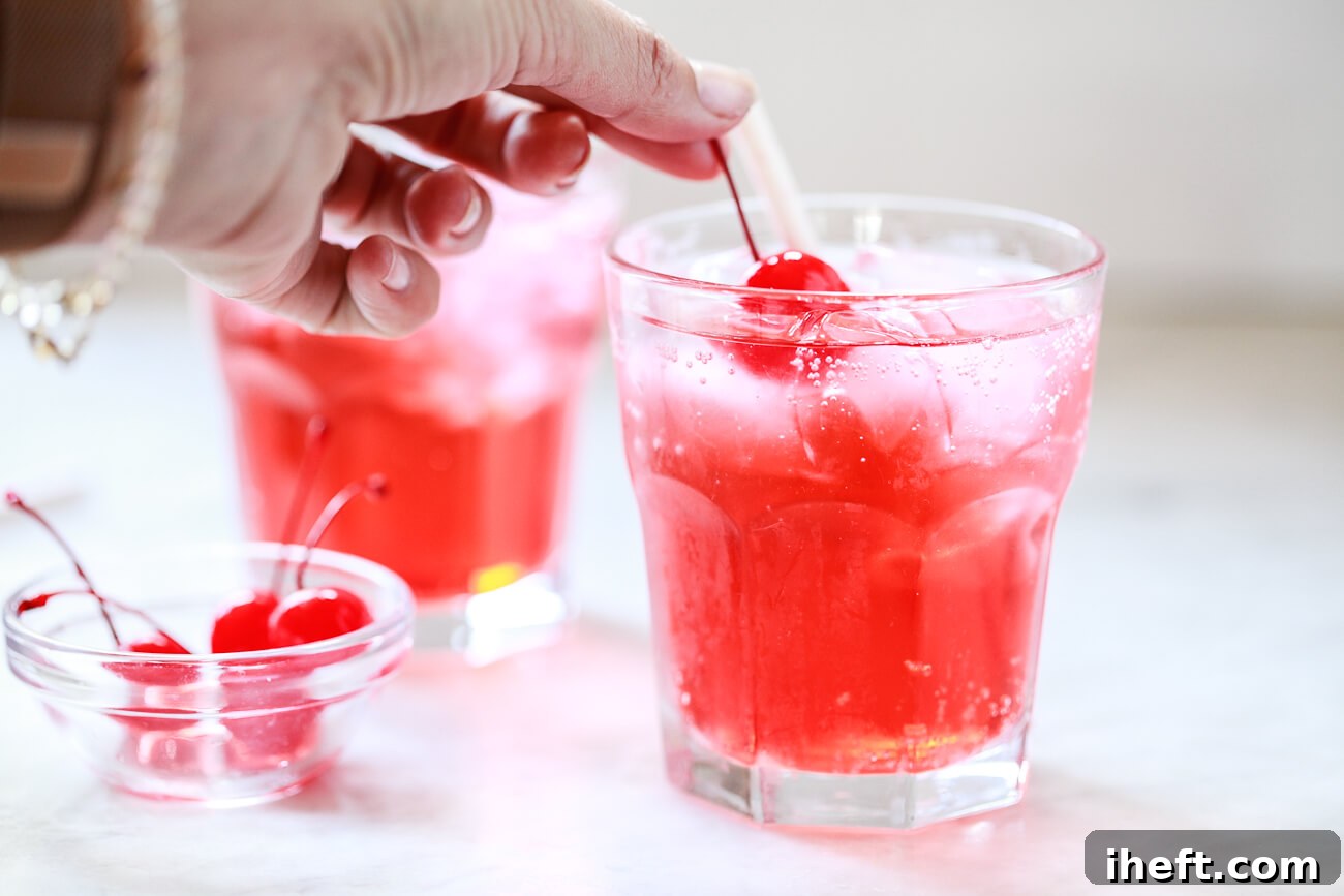 A bright red maraschino cherry is carefully placed into a finished Shirley Temple drink, adding the classic garnish.