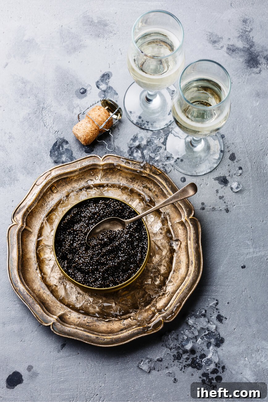 A beautiful overhead photo of caviar on a bowl of crushed ice on a silver platter. Two glasses of Champagne sit on the side. 