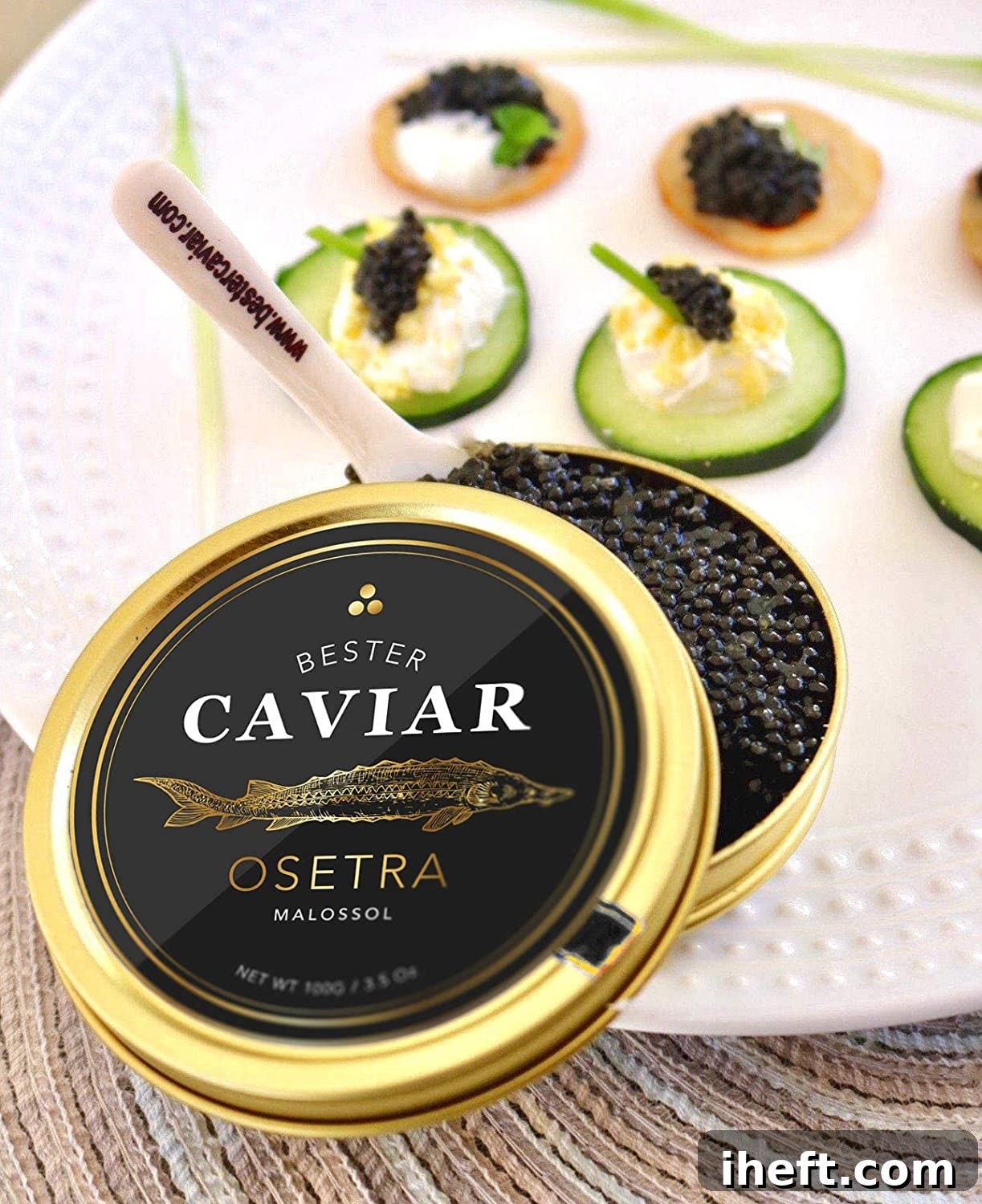 A gold tin of Osetra caviar with a small spoon and canapes in the background. 