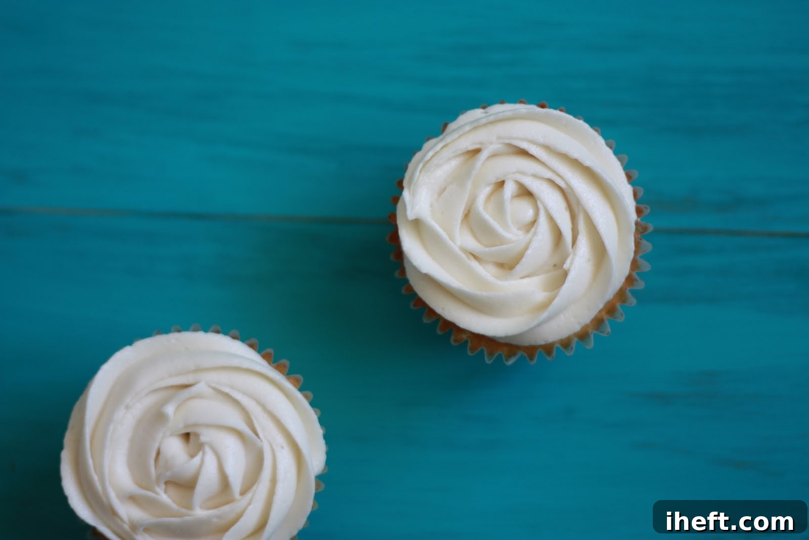 Close-up of freshly piped rose frosting on multiple vanilla cupcakes arranged beautifully.