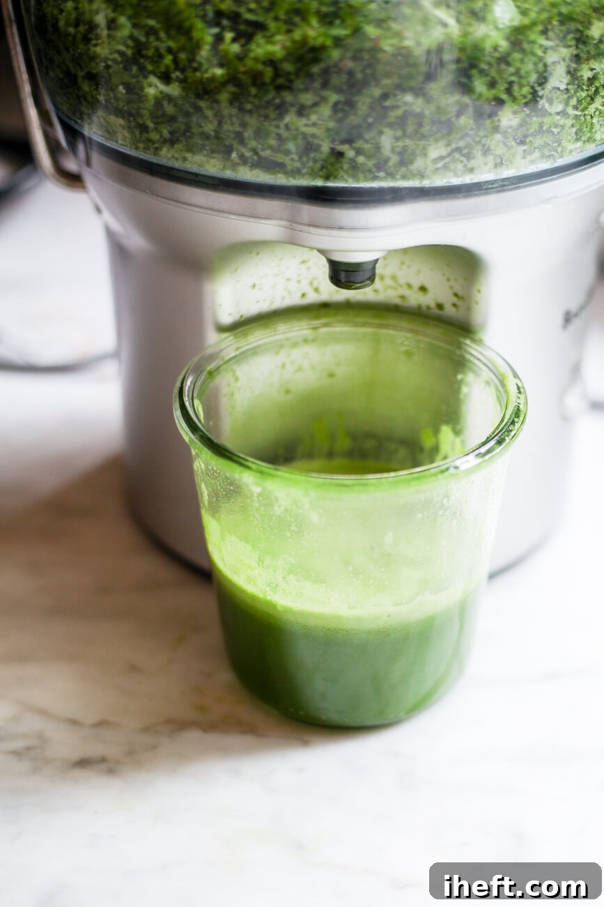A elegant Weck jar filled with freshly pressed vibrant green juice and ice sits on a pristine marble countertop, positioned directly beneath a juicer.