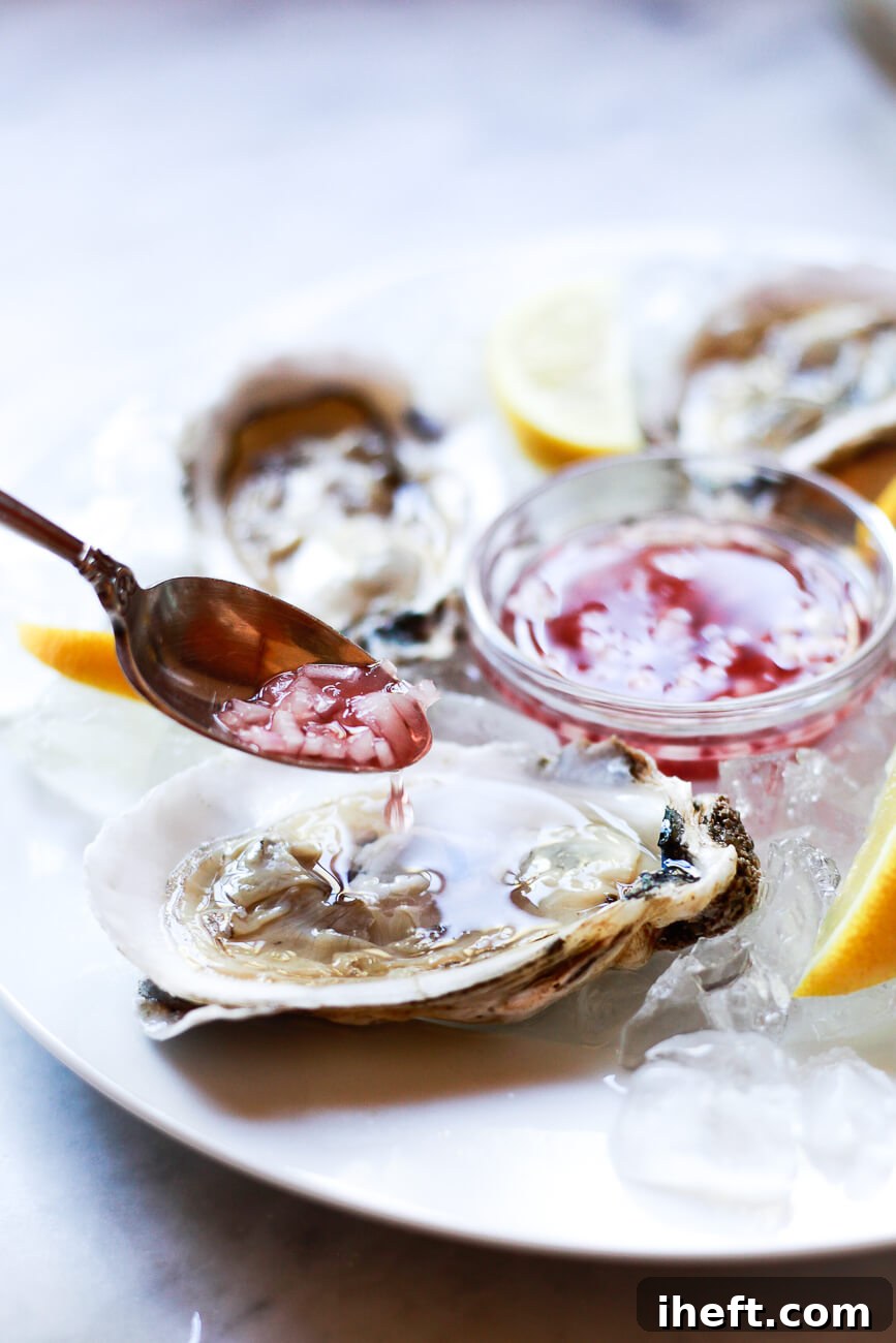 A small spoon of shallot mignonette sauce is spooned over a raw oyster on the half shell.