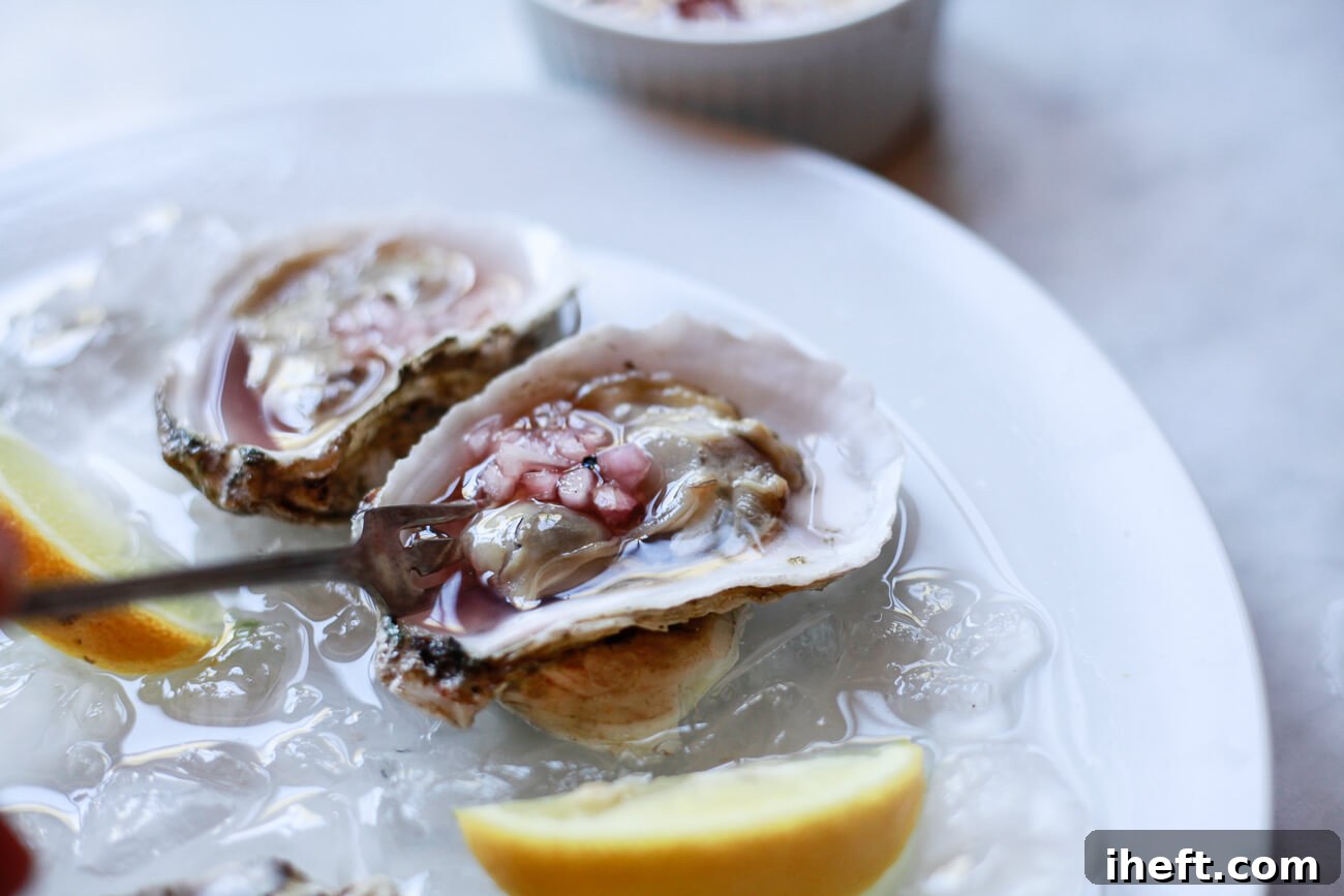 A raw oyster topped with mignonette is scooped out with a small fork.