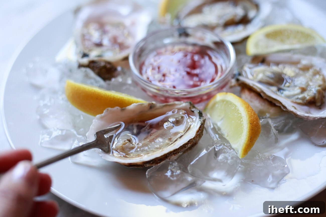 A small, elegant fork is poised, scooping up a glistening raw oyster from its half shell, ready for consumption. 