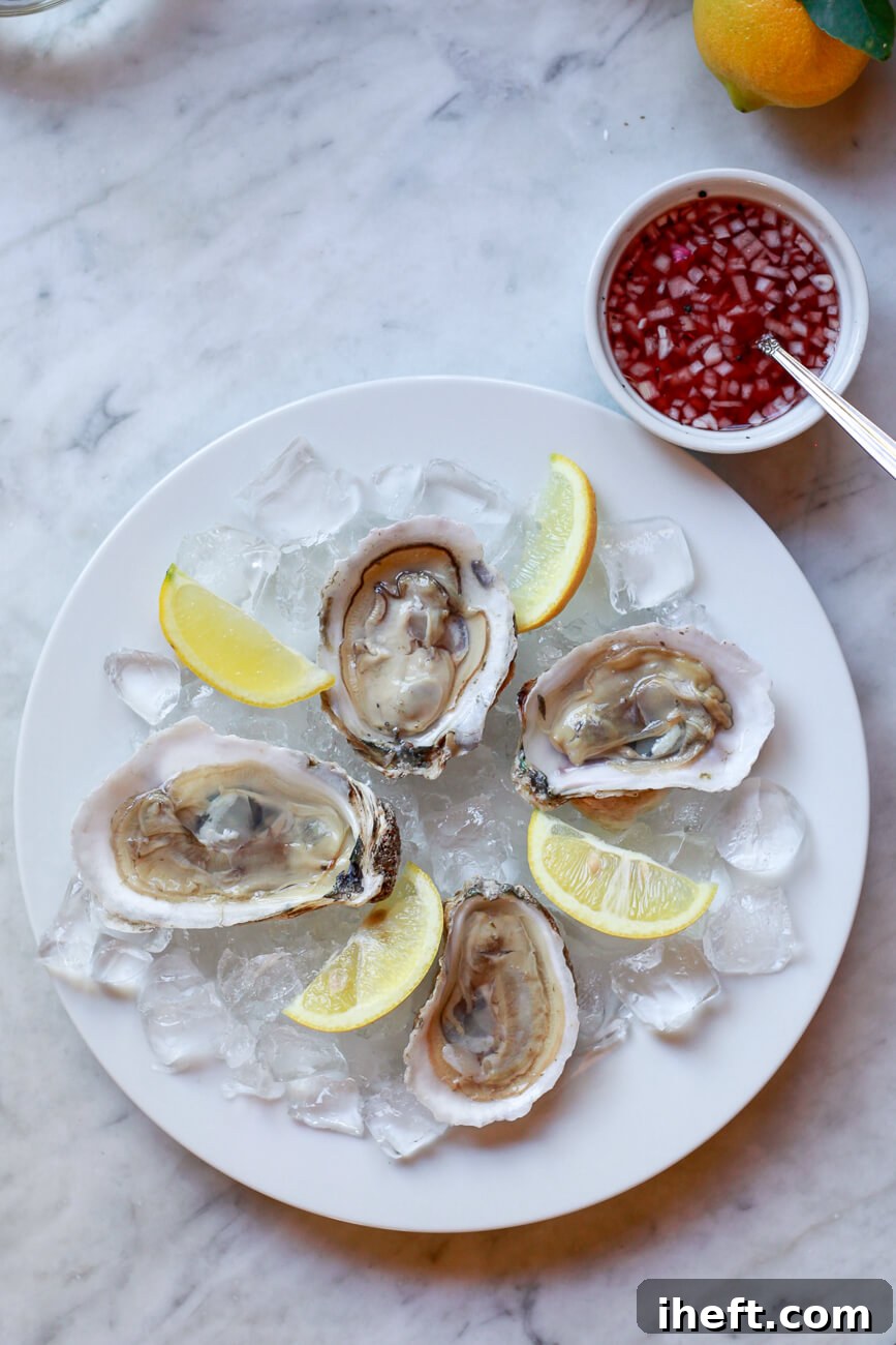 Four perfectly shucked raw oysters on the half shell are elegantly presented on a bed of crushed ice, garnished with fresh lemon wedges and a small bowl of classic mignonette sauce on the side.