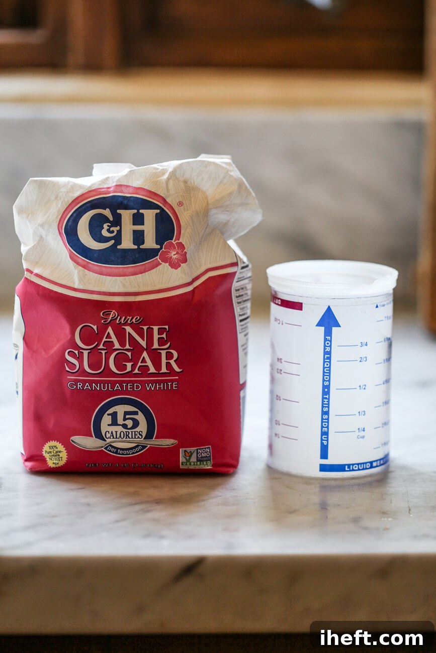 A bag of C&H white sugar and a cup of water sits on a marble countertop before making hummingbird nectar.