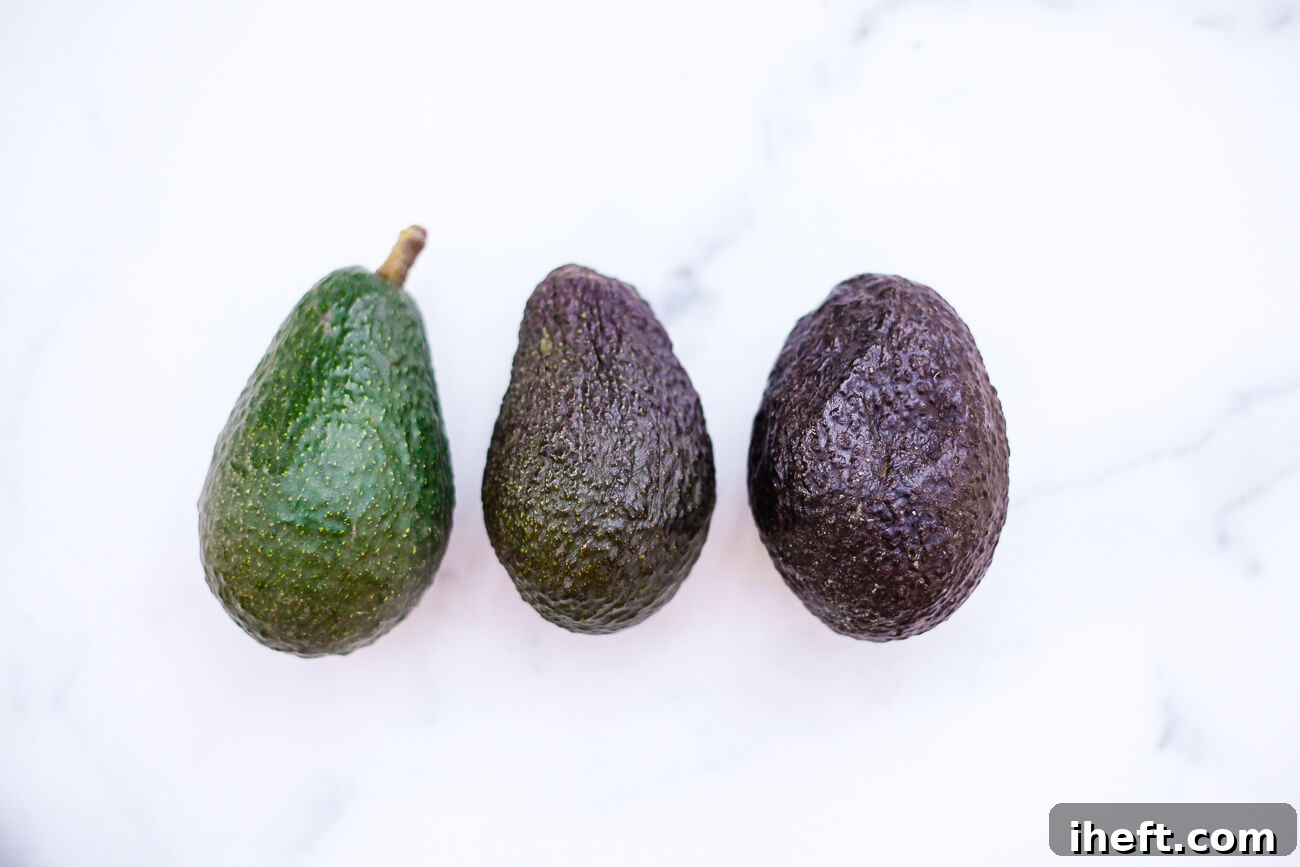 Three avocados of varying ripeness on a white marble background. 