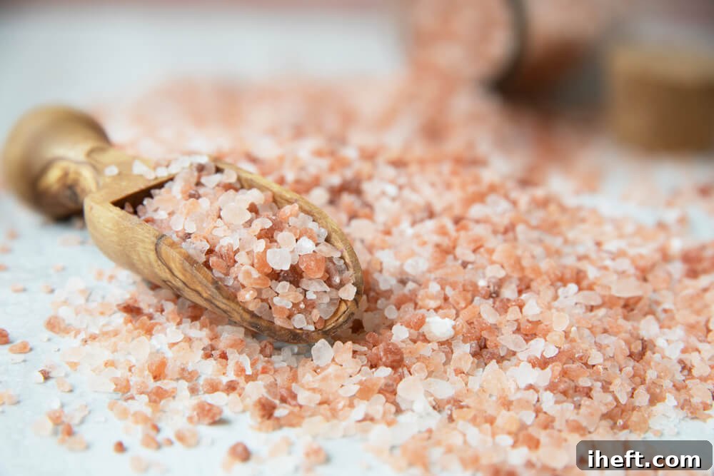 A close-up photo of pink Himalayan Salt granules with a small wooden scoop.