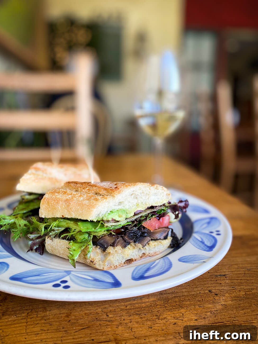 A beautifully composed vegan portobello mushroom sandwich featuring fresh lettuce, creamy avocado, and ripe tomato, served on a stylish blue and white plate set on a rustic wooden table.