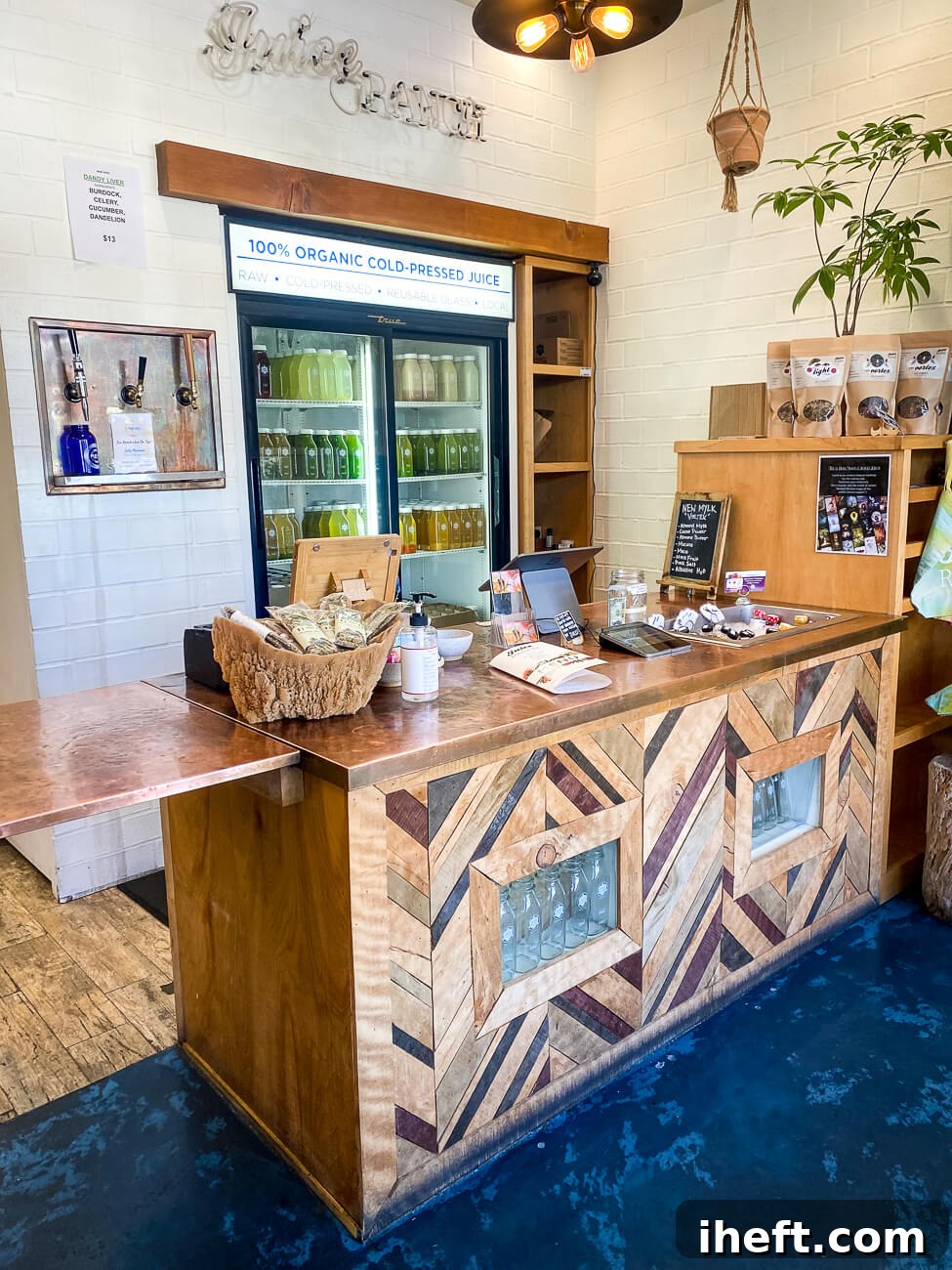 The clean and inviting interior of Juice Ranch in Santa Barbara, featuring a sleek wooden bar counter in the foreground and a sparkling glass case brimming with colorful, organic cold-pressed juices in the background.