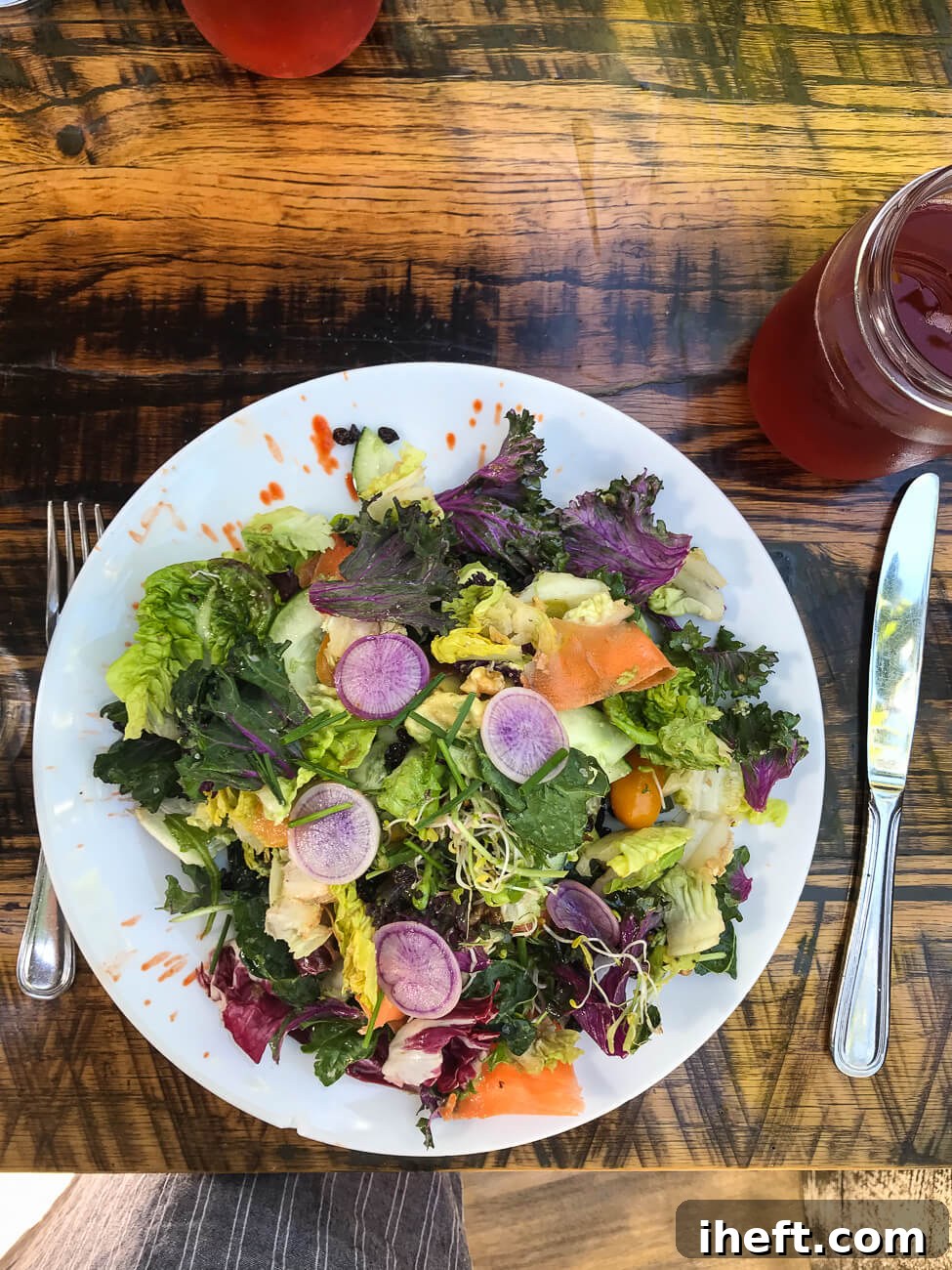 A vibrant, generously sized salad featuring purple radish slices, artfully arranged on a rustic wooden table at Mesa Verde, a former vegan restaurant in Santa Barbara.