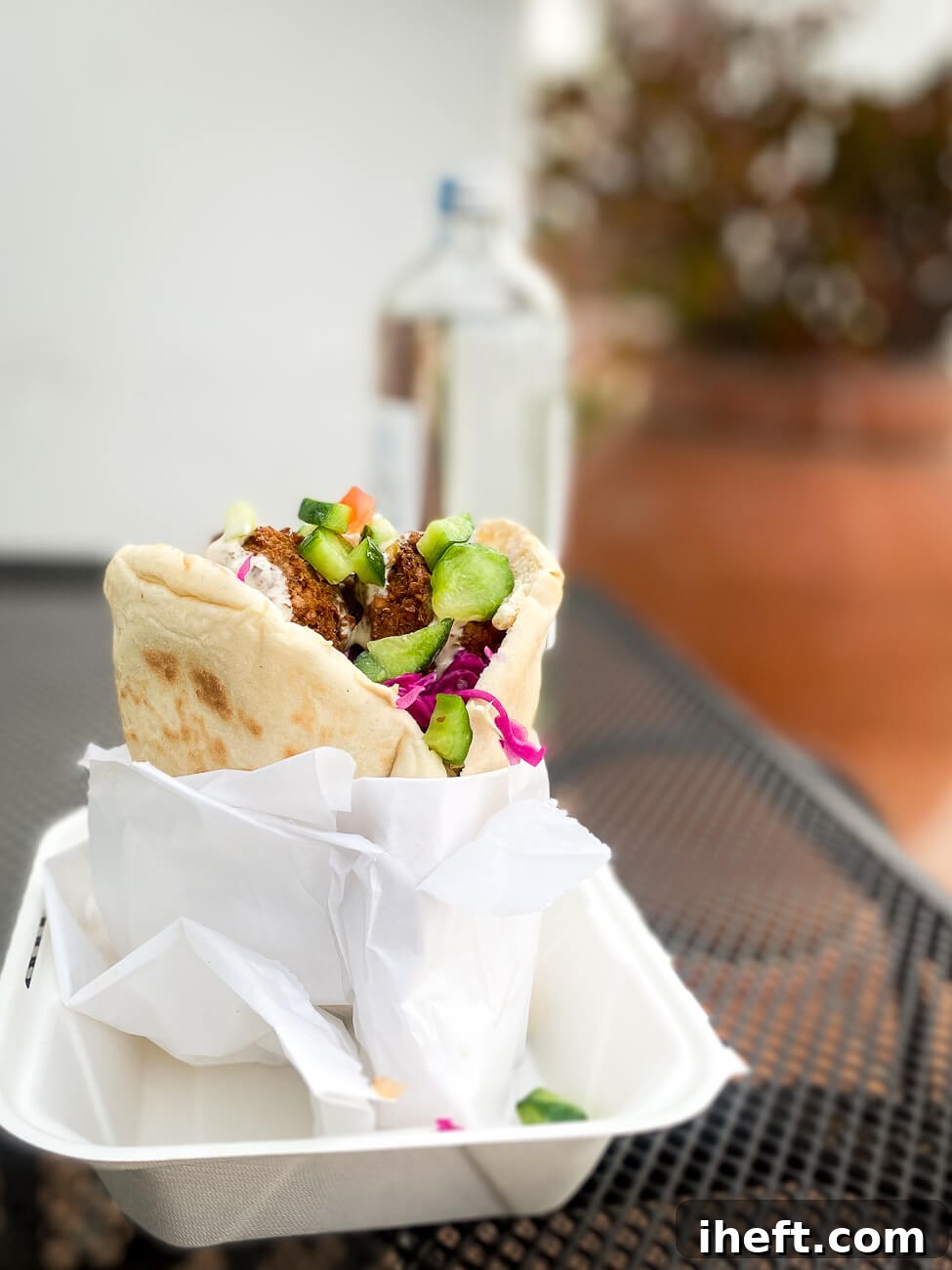 A delectable falafel sandwich, perfectly assembled and presented on an inviting outdoor patio table, from Falabar, a renowned vegan restaurant in Santa Barbara.