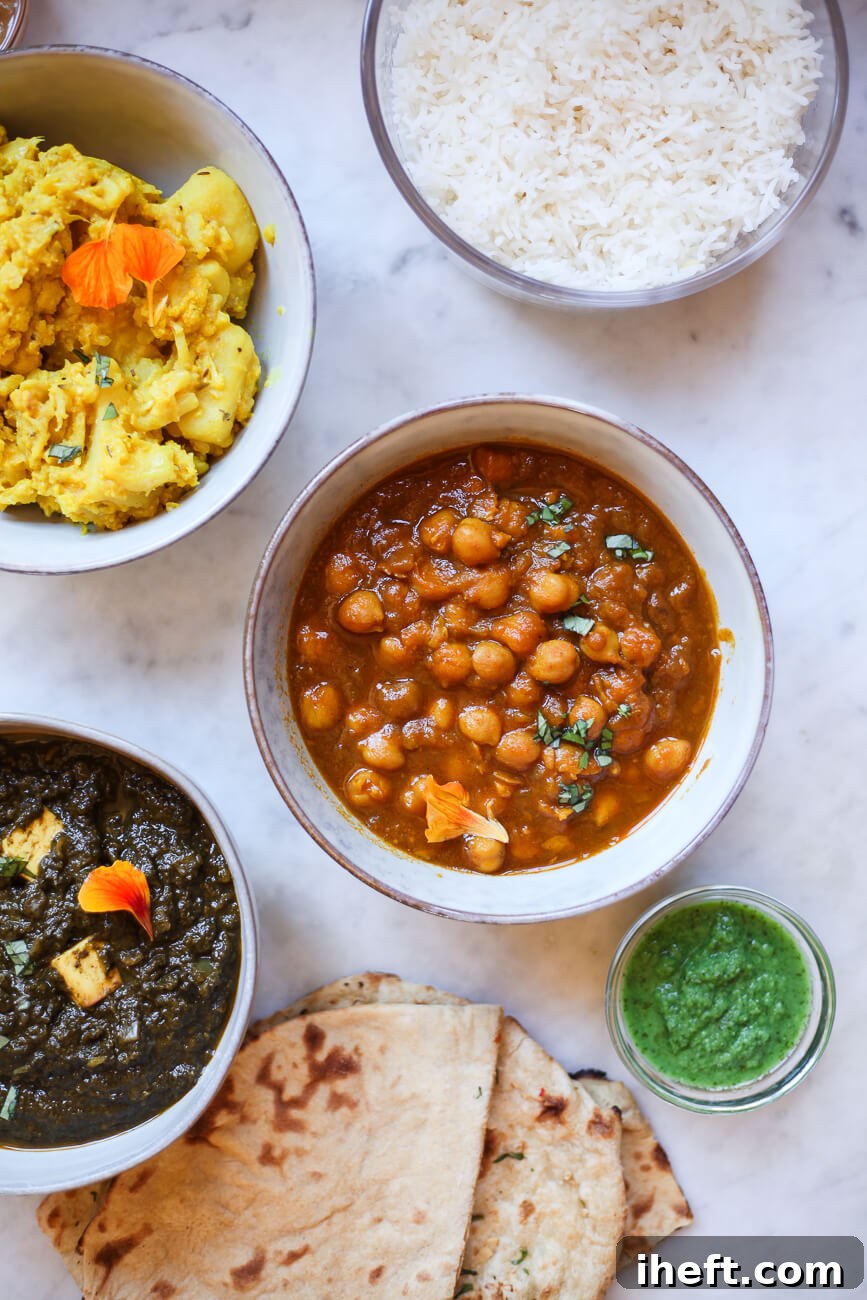 A collection of ceramic bowls filled with vibrant and aromatic vegetarian Indian dishes. Clockwise from top, Aloo Gobhi, fluffy Basmati rice, rich Chana Masala, refreshing mint chutney, soft Chapati bread, and creamy Saag.