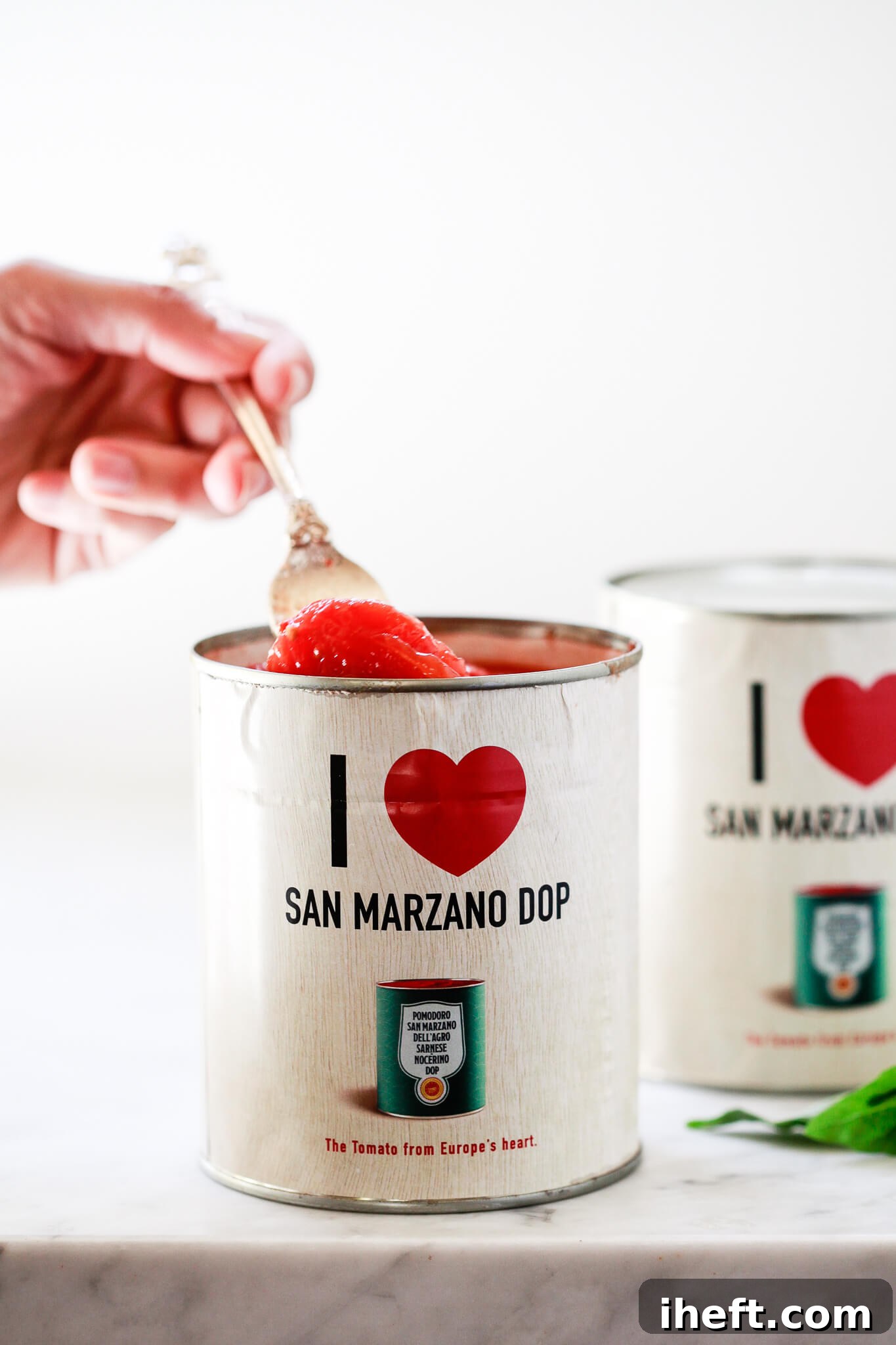 A whole peeled tomato is pulled out of a San Marzano DOP can with a fork.