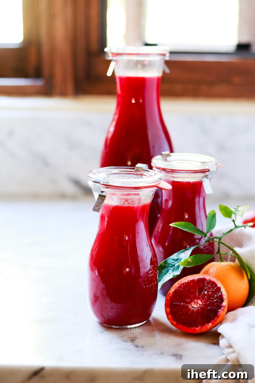 One large and two small Weck juice jar carafes filled with red blood orange juice on a white marble kitchen counter.