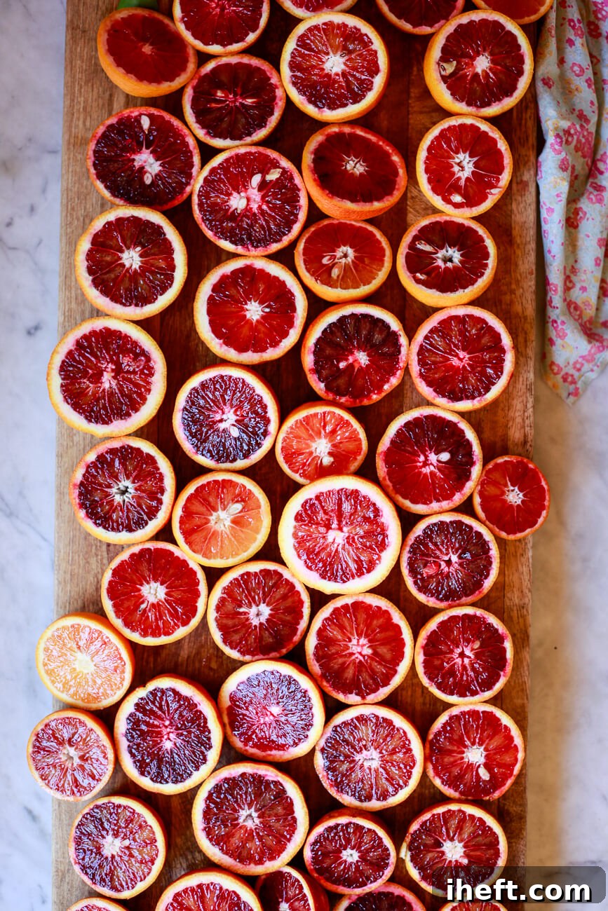 A large wooden cutting board filled with many red blood orange halves.