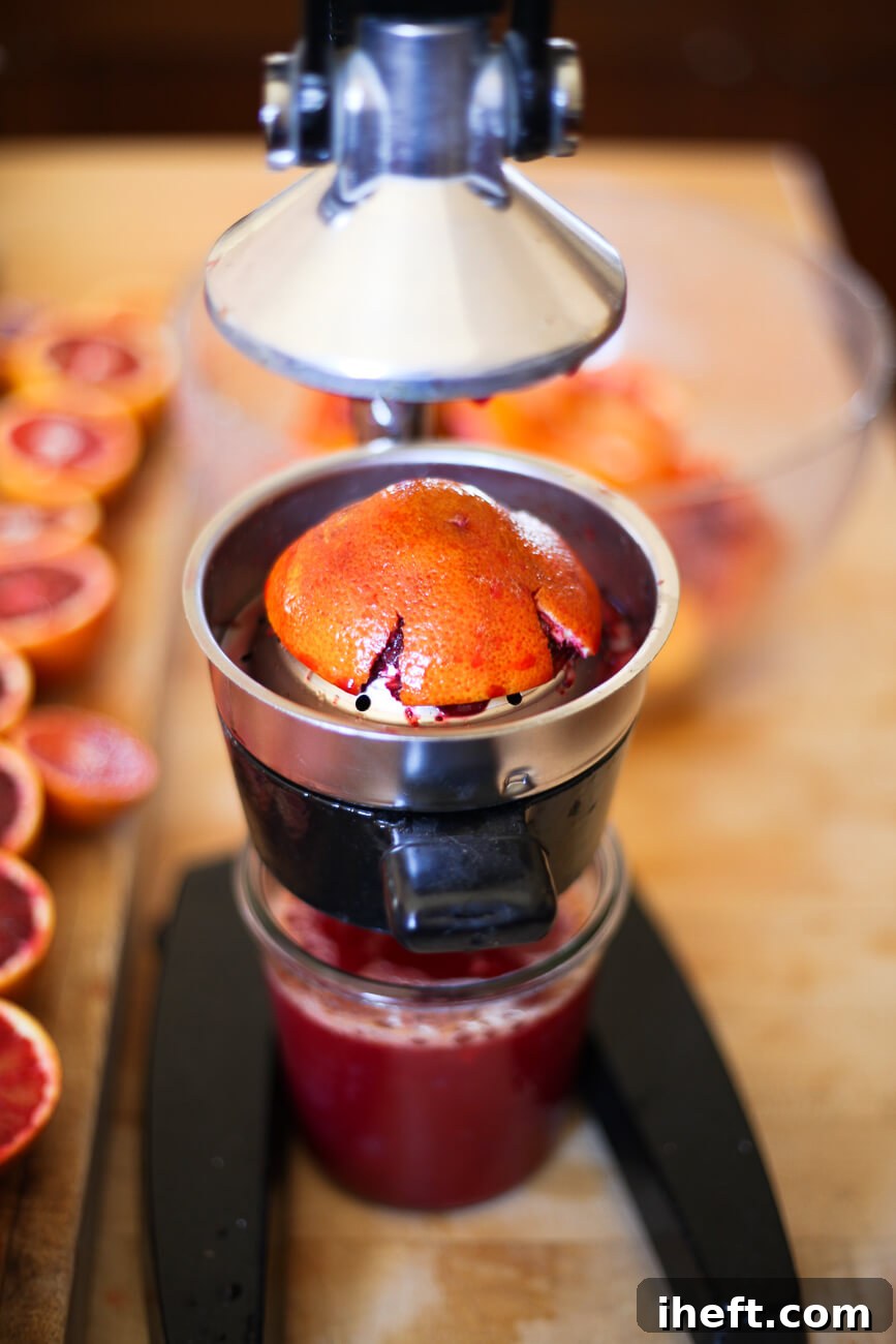 Half of a blood orange is pressed in a manual citrus press.
