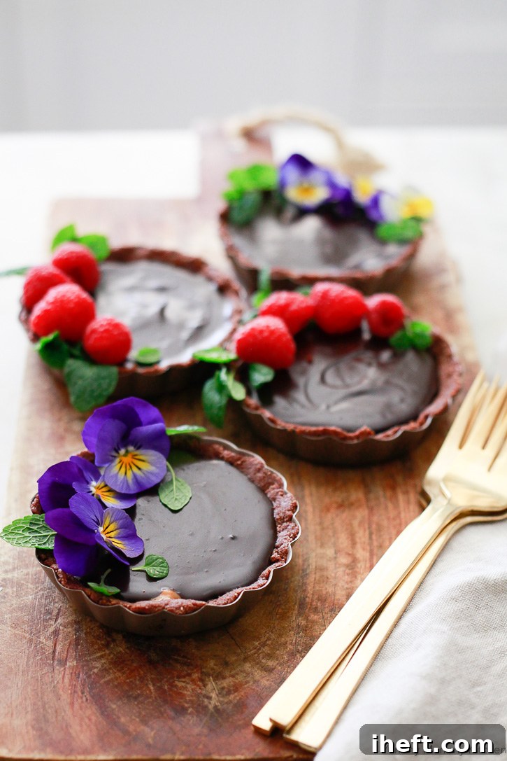 Beautiful chocolate tarts topped with edible flowers, fresh raspberries, and vibrant mint leaves. These decadent tarts, inspired by Hail Merry, are vegan, gluten-free, and paleo-friendly.