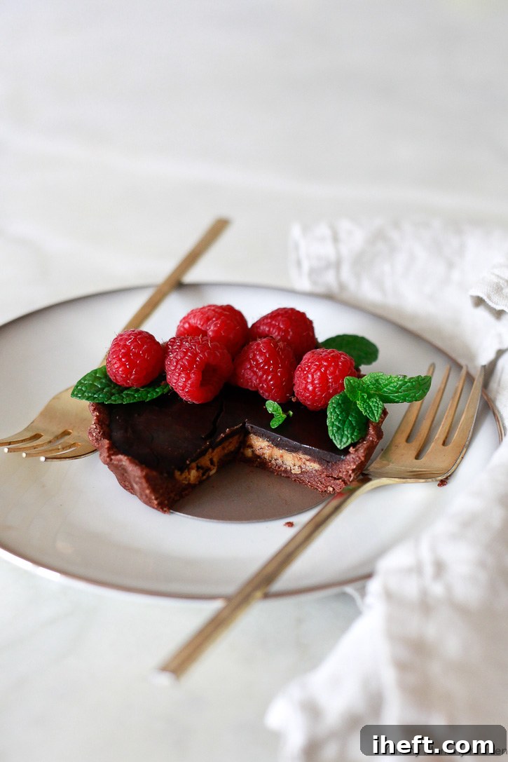 A cross-section view of a delicious no-bake chocolate peanut butter cup tart, revealing its three distinct, creamy layers. This healthier version is vegan, gluten-free, and paleo-friendly.
