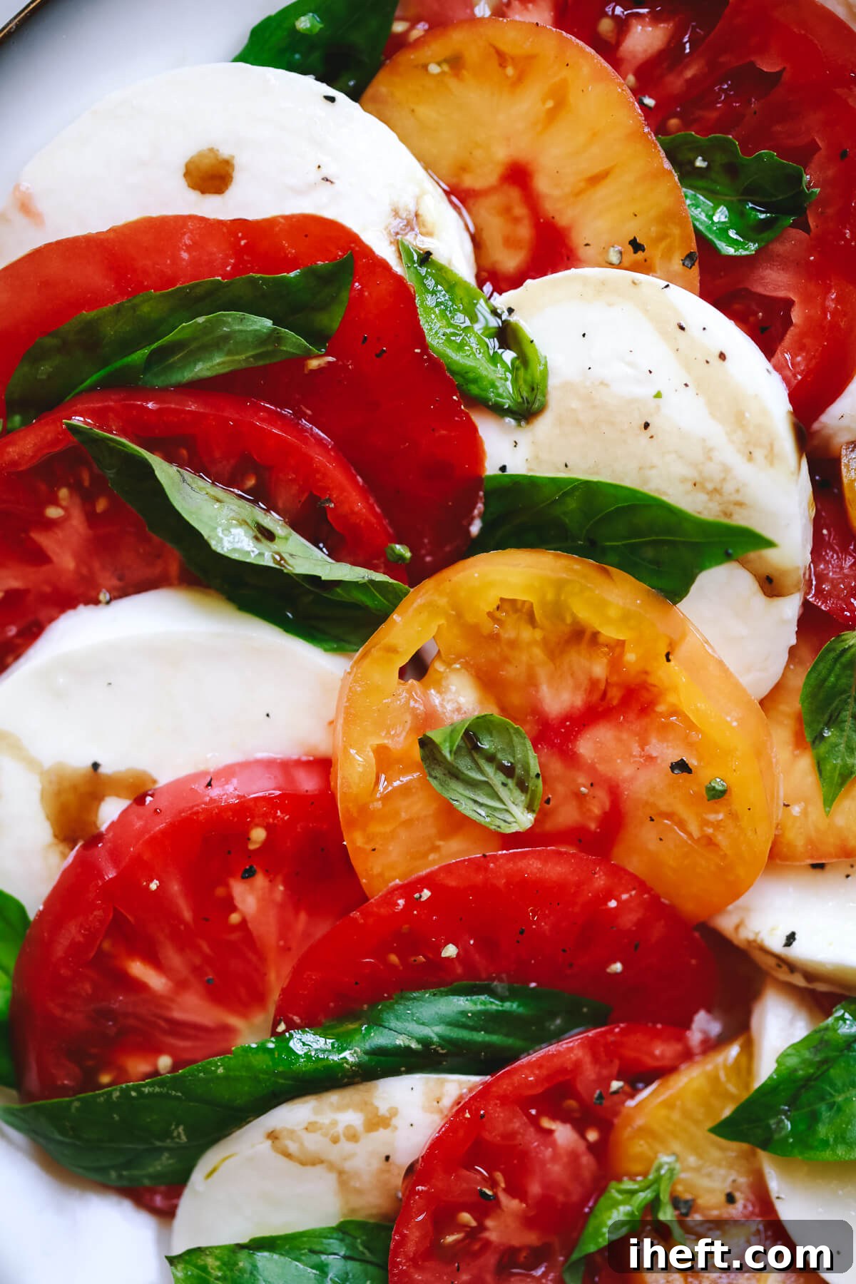 A close-up photo of a vibrant heirloom tomato Caprese salad, artfully arranged with creamy mozzarella and fresh basil leaves, showcasing a perfect fresh tomato recipe.
