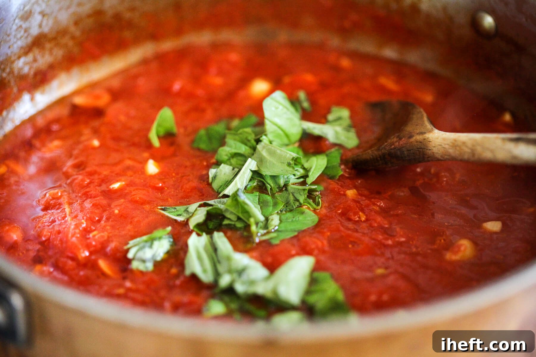 San Marzano marinara sauce topped with fresh basil in a skillet with a wooden spoon.