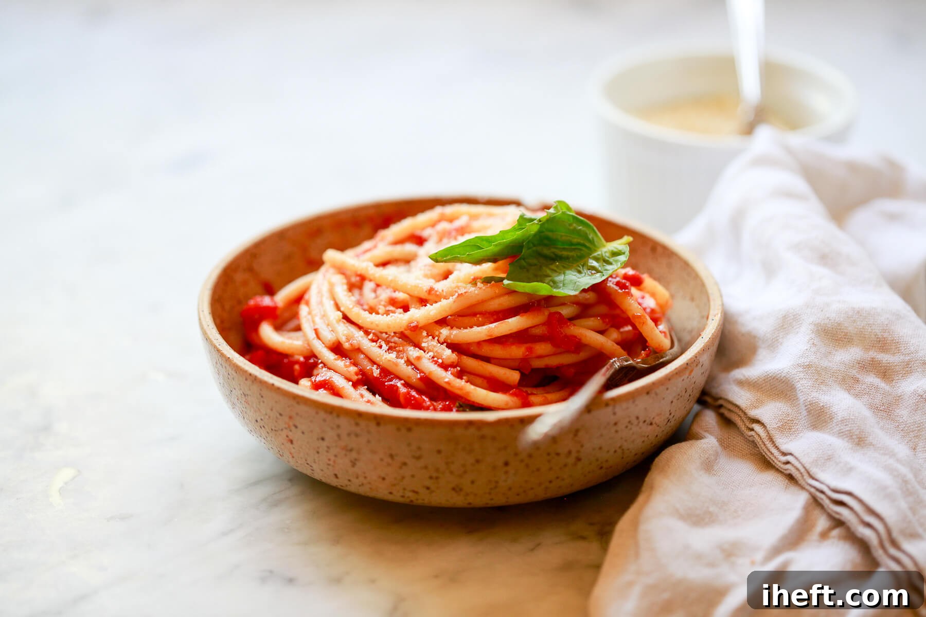 Spaghetti with San Marzano tomato sauce in a ceramic bowl topped with basil.
