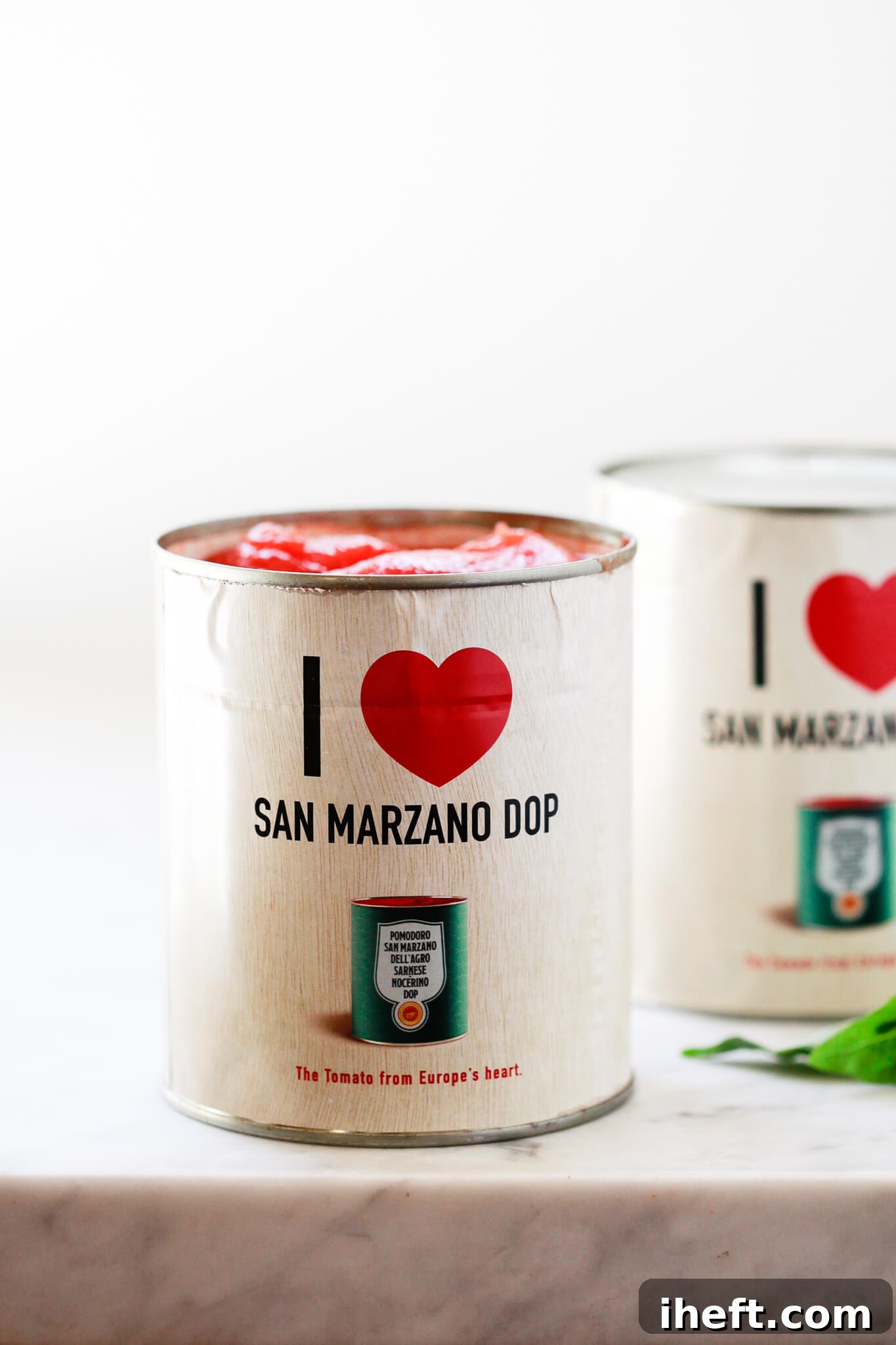 An opened can of 'I love San Marzano DOP' tomatoes rests on a pristine white marble countertop, showcasing the quality of the product.