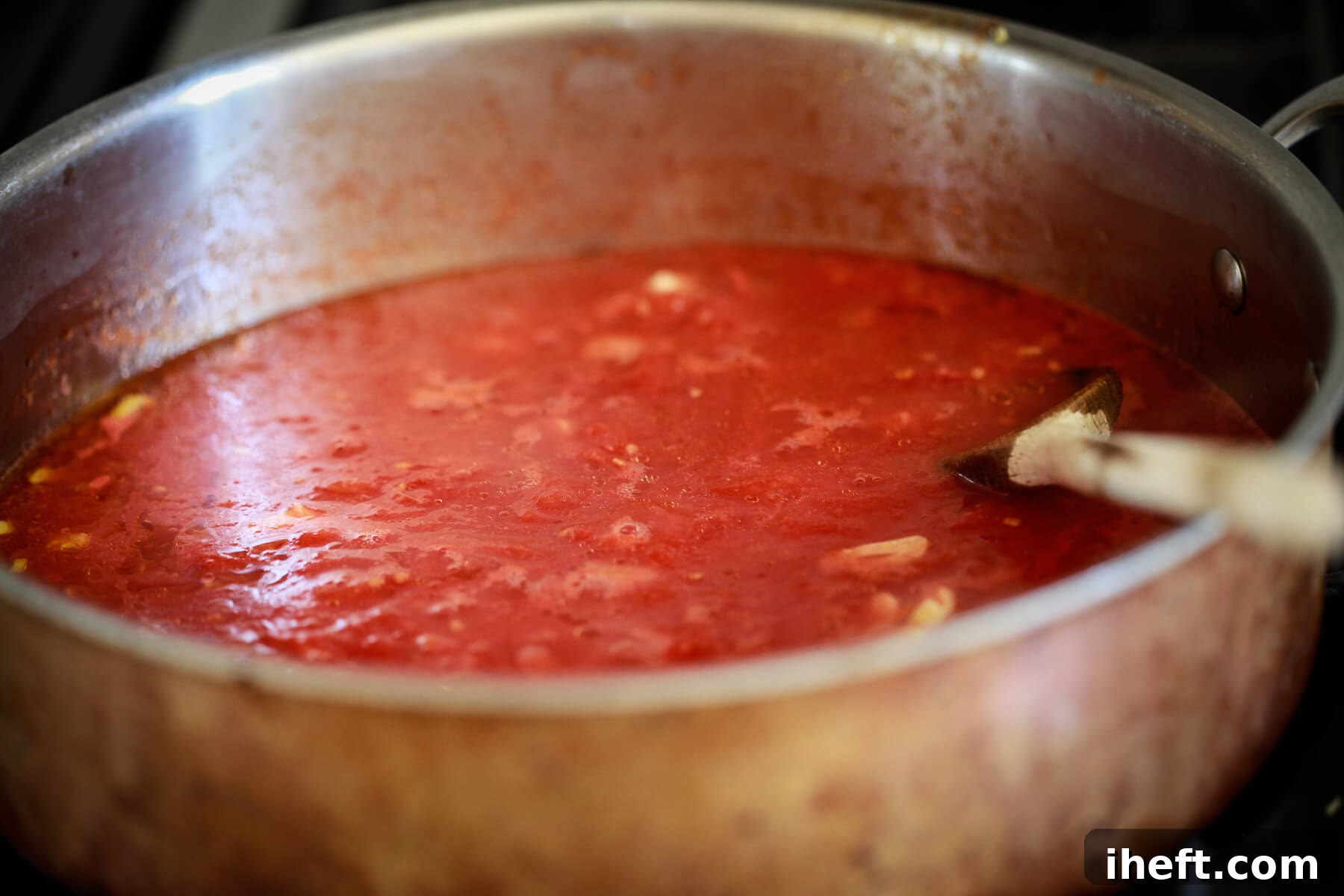 A skillet filled with San Marzano tomato sauce simmering on a stove.