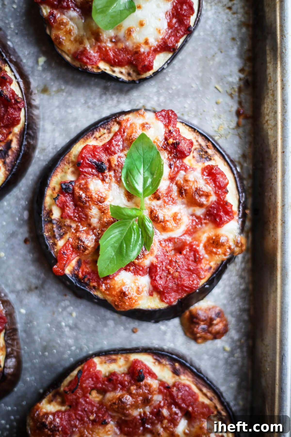 An overhead close-up photo of a mini eggplant pizza round topped with tomato sauce, cheese, and basil.