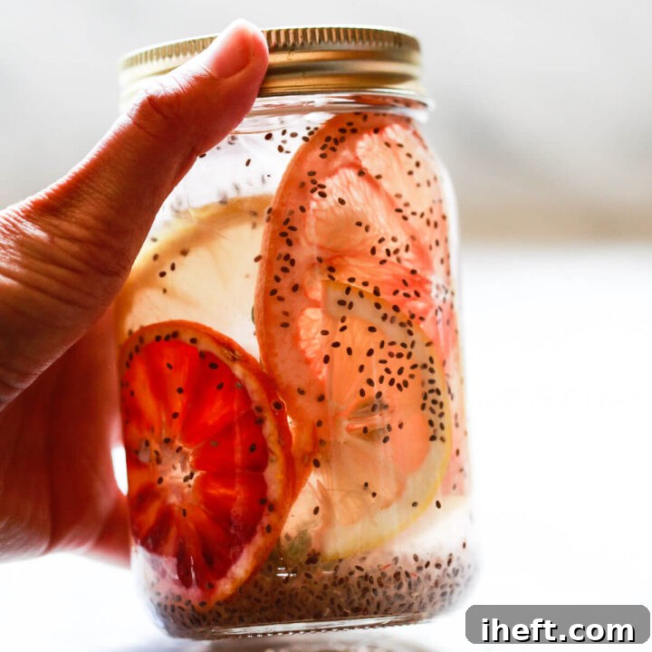 A mason jar filled with chia seeds in water with citrus slices gets picked up from a marble countertop.