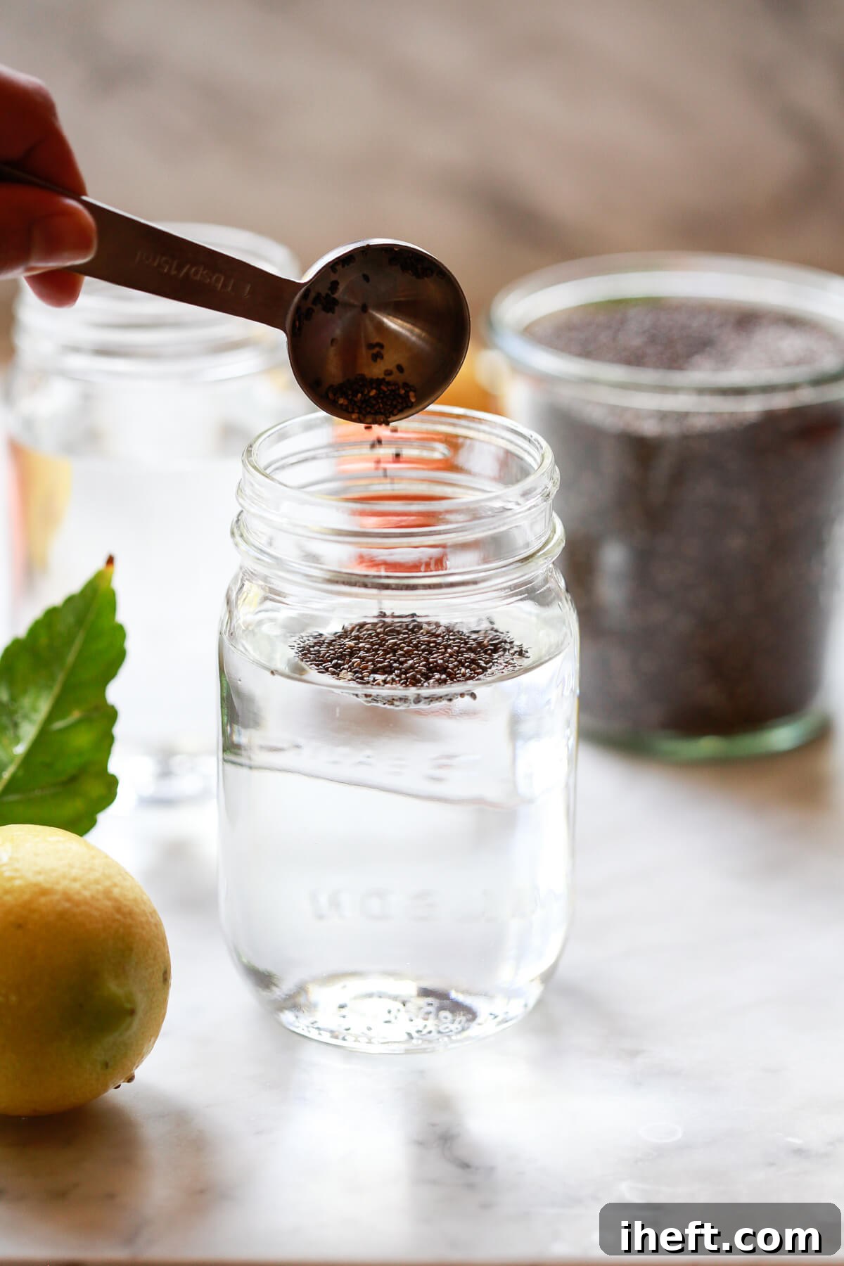 A tablespoon of chia seeds being added to a mason jar filled with water, illustrating the first step in making a chia drink.