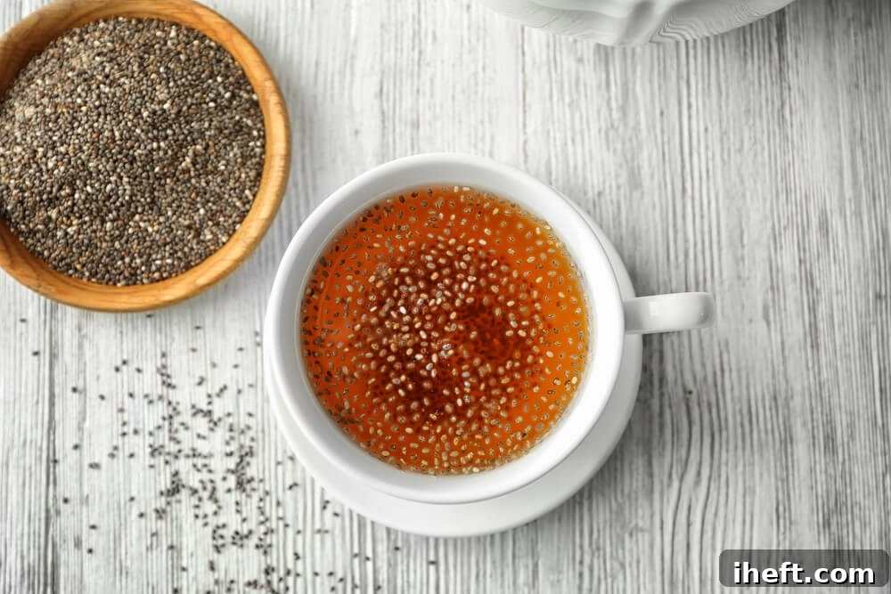 A white ceramic mug filled with herbal tea and chia seeds sits on a white wooden counter, next to a small bowl of dry chia seeds.
