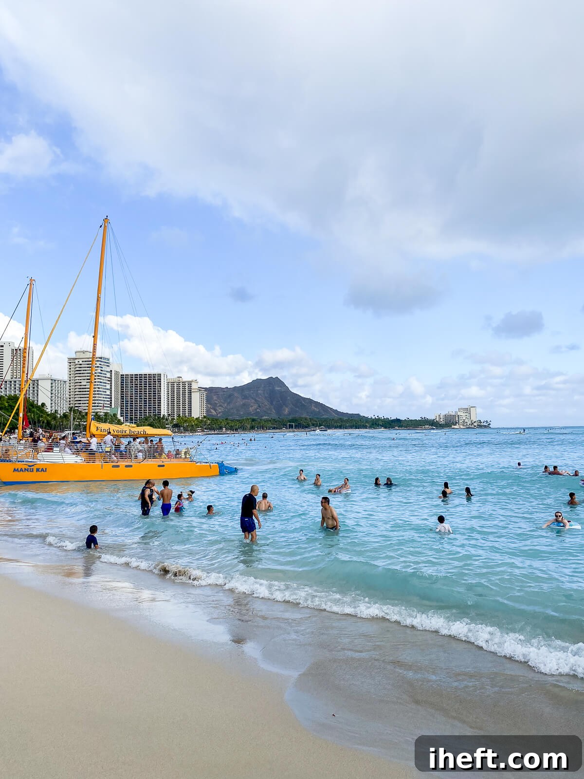 Beachgoers swim and play in the turquoise water on Waikiki beach with Diamond Head in the background. 