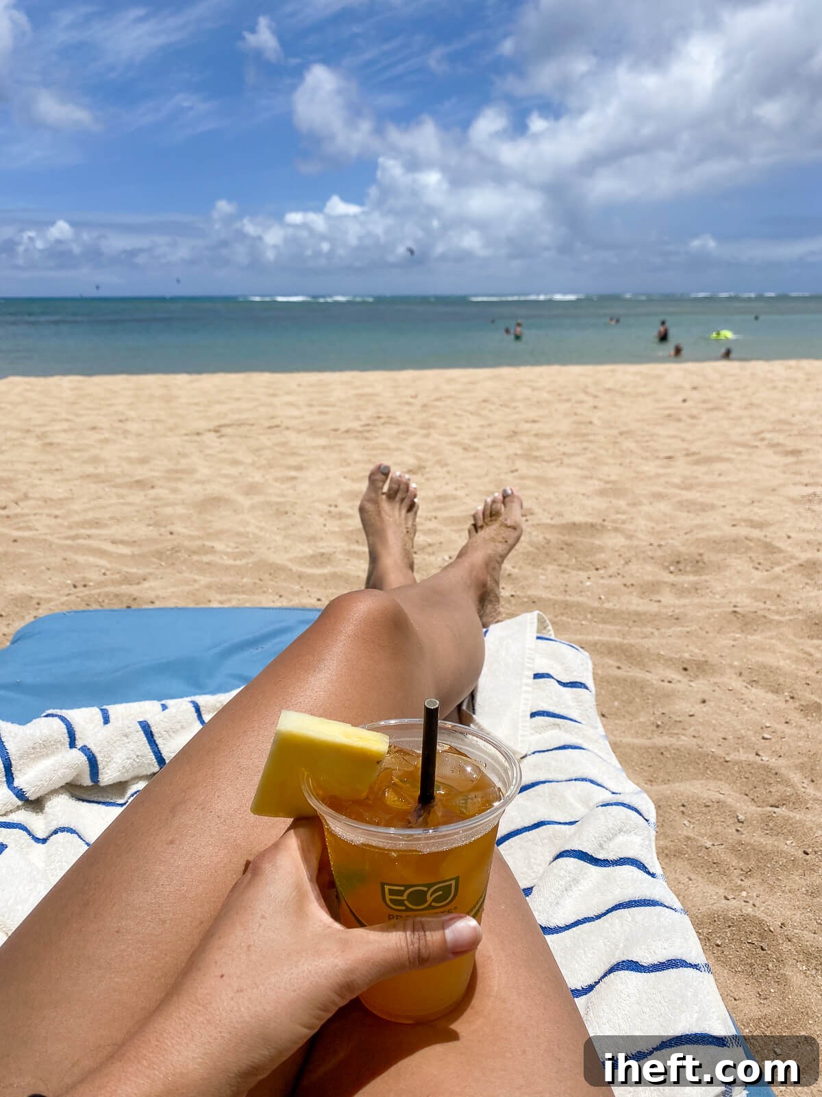 A woman's hand holds a mai tai garnished with a pineapple on Kahala Beach. 