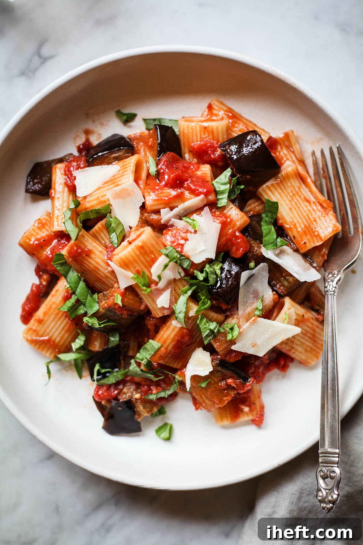 A white ceramic pasta bowl filled with Pasta alla Norma eggplant ragu on rigatoni. 