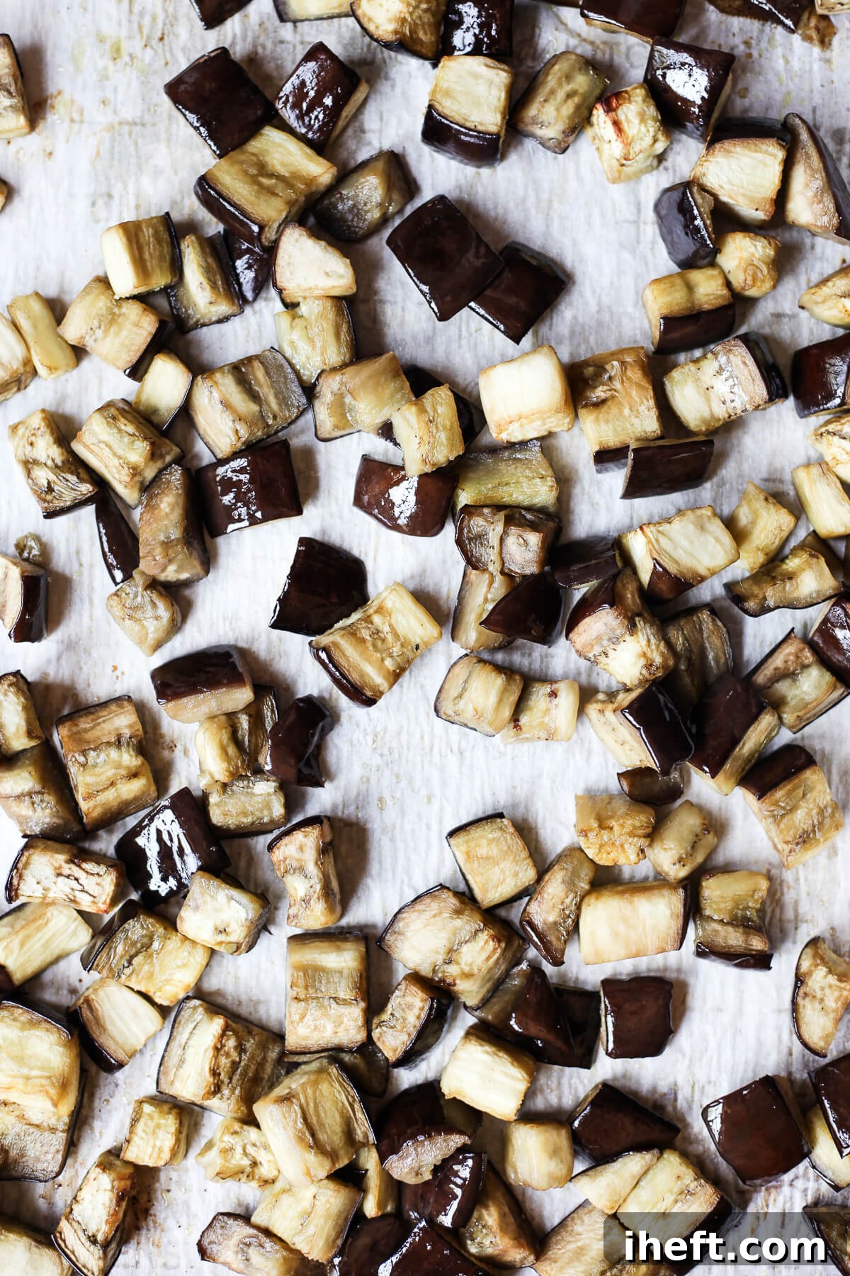 Cubes of baked eggplant on a parchment-lined baking sheet. This roasted eggplant will be used for eggplant ragu. 