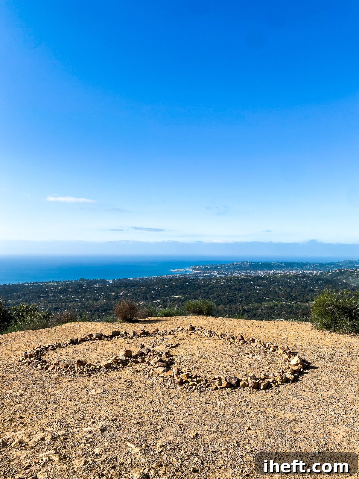 The view from the top of a mountain during a hike in Santa Barbara. A heart is made out of rocks on the ground and the ocean is seen in the background. 