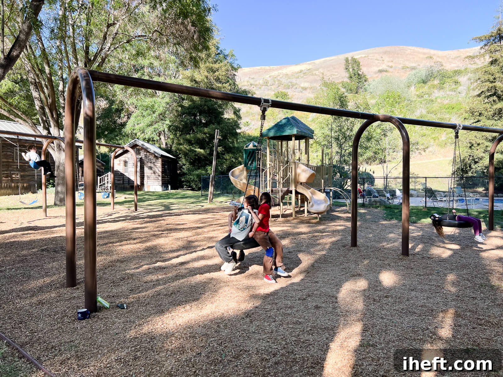 Kids laughing and playing on a tire swing at the vibrant playground of the El Capitan Canyon resort, capturing a moment of pure joy and outdoor fun.