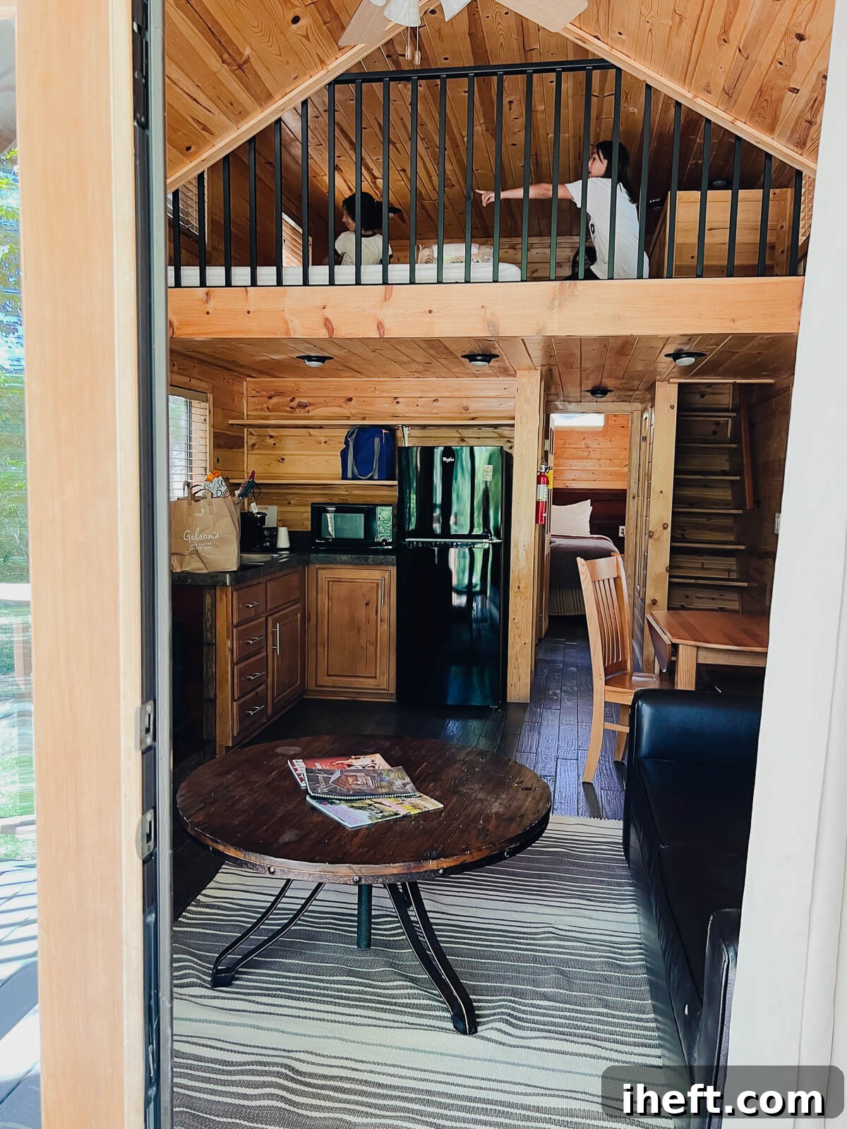 A candid look into the interior of a spacious Corral Loft cabin at El Capitan Canyon, showcasing two pre-teen girls happily playing in the cozy loft area above the well-equipped kitchen, highlighting the family-friendly design of the cedar cabin.