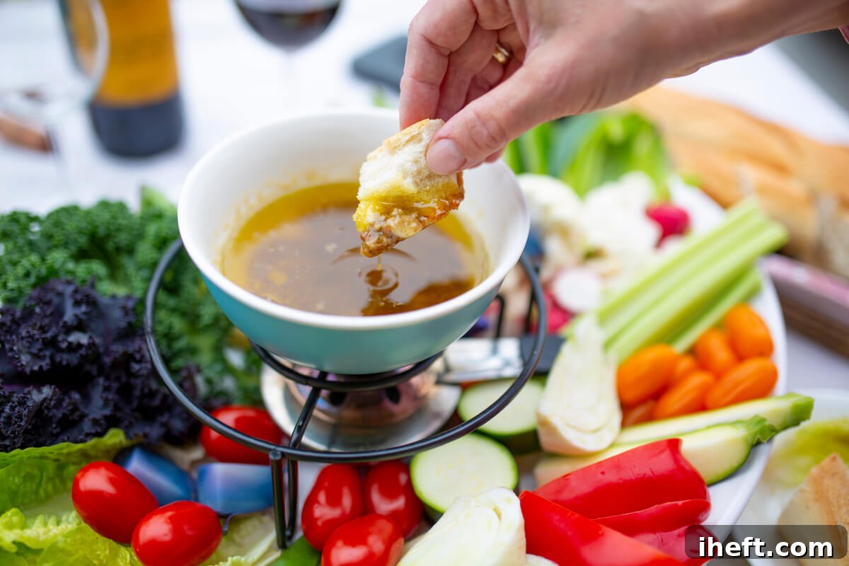 A woman's hand gracefully dips a piece of bread into a small, warm bowl of Bagna Cauda, artfully placed above a platter of crisp vegetables, evoking a communal dining experience.