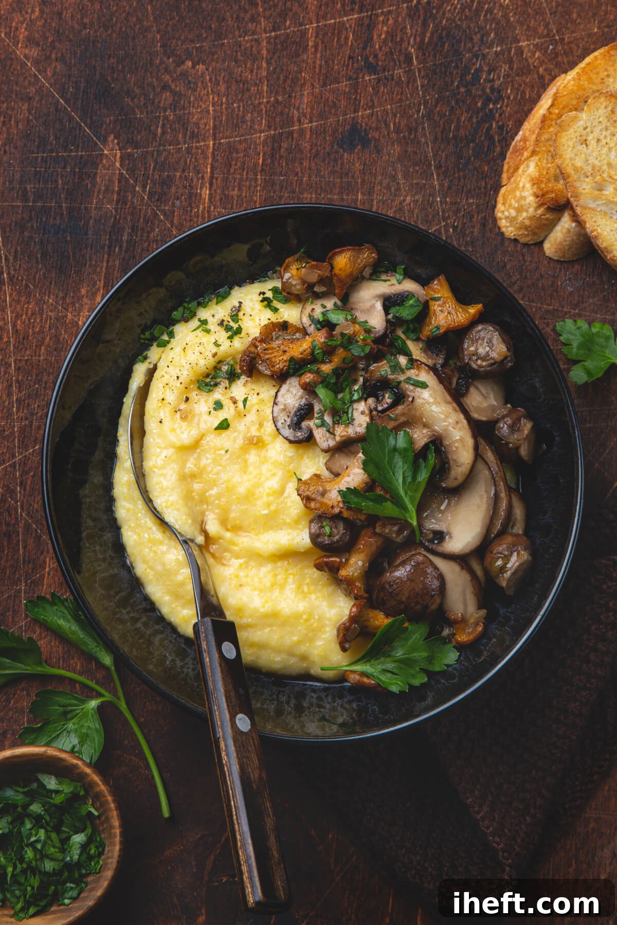 A dark bowl filled with creamy polenta, elegantly topped with sautéed mushrooms and fresh parsley, resting on a dark wooden counter.