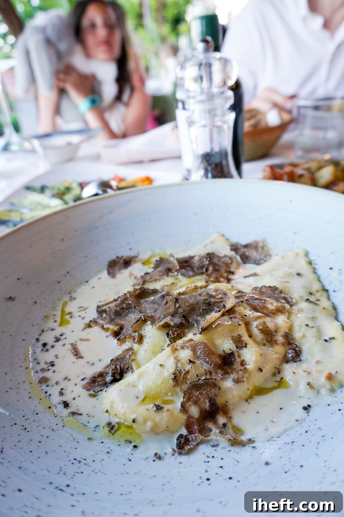 A pristine white ceramic bowl holding three mezzelune ravioli, exquisitely topped with a delicate cream sauce and fragrant black truffle shavings.