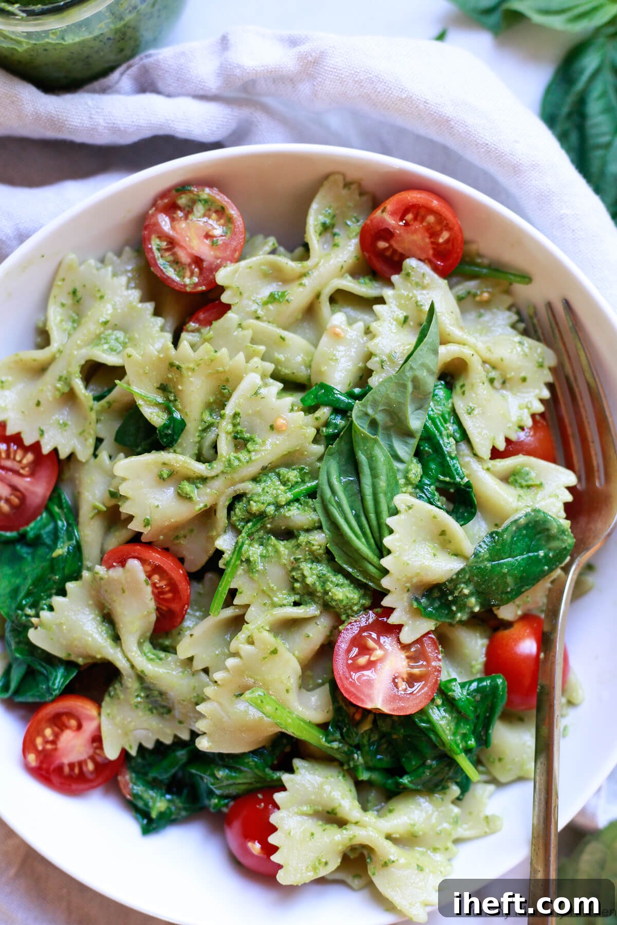 Bowtie pasta generously coated with vibrant green pesto, adorned with fresh basil leaves and halved cherry tomatoes, a typical Ligurian Italian food.