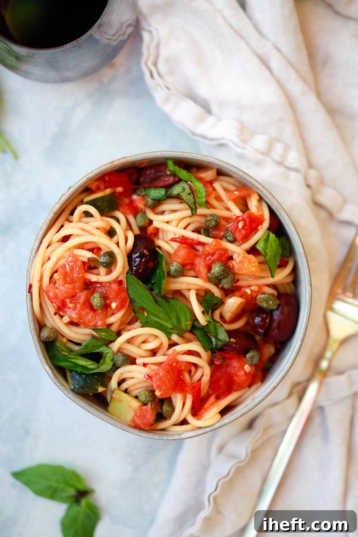 A grey bowl filled with robust spaghetti alla Puttanesca, rich with tomatoes, capers, olives, and garlic, a symphony of Mediterranean flavors.
