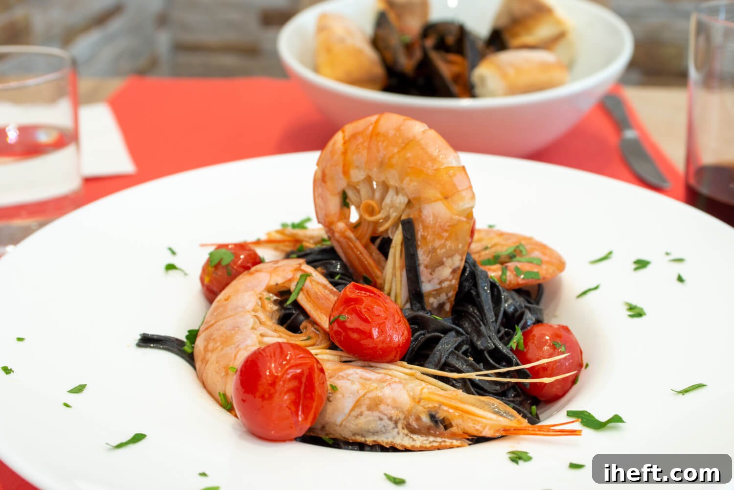 Dark black squid ink pasta on a white plate, elegantly topped with whole prawns and vibrant cherry tomatoes, creating a striking contrast.