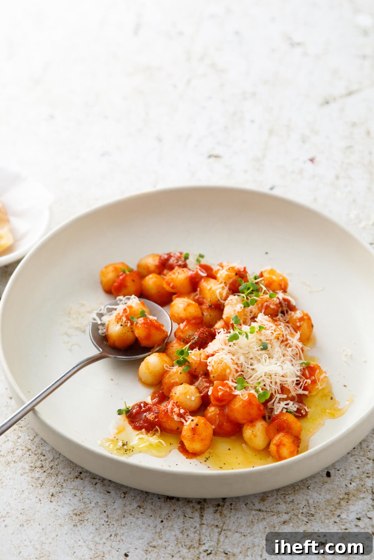 A pristine white ceramic pasta bowl filled with small, tender gnocchi bathed in a rich tomato sauce and finished with a sprinkle of shredded cheese.