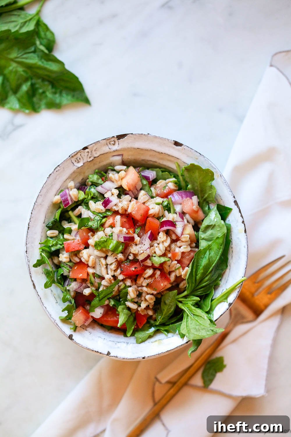 A white ceramic bowl filled with a vibrant Tuscan farro salad, featuring fresh tomatoes, crisp red onion, fragrant basil, and peppery arugula.
