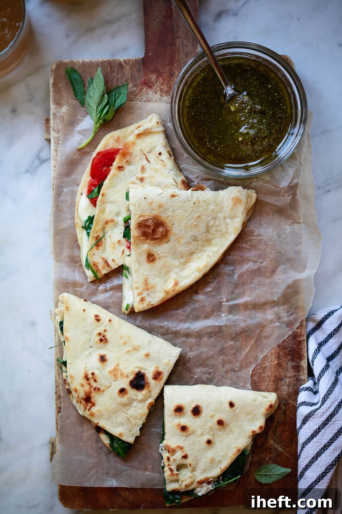 A piadina filled with melted mozzarella and ripe tomatoes, artfully cut into triangles on a wooden cutting board, with a side bowl of pesto.