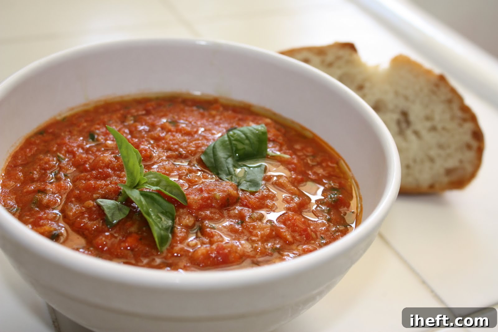 A pristine white bowl filled with rich Pappa al Pomodoro, a rustic Italian bread and tomato soup, elegantly topped with fresh basil.
